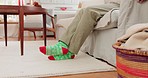 Christmas, cozy and legs of a person with socks on feet for winter on living room sofa. Couch, comfy and person in the lounge with festive clothes for xmas, festive and relax in a home during holiday