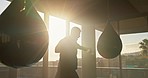 Boxer, fitness and man boxing with punching bag in gym at home, cardio training workout with sun and lens flare. Silhouette, athlete and sports, strong and fast with skill and healthy exercise.