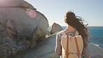 Beach, travel and woman is walking on rocks, adventure and ocean hiking or vacation with backpack. Nature, sea and holiday outdoor with female back view, journey and wellness with peace and calm.