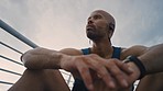 Relax, fitness and man in headphones thinking of running exercise, cardio workout or marathon training in a city. Sports, freedom and tired athlete runner resting on a break or relaxing on a bridge