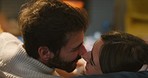 A young couple kissing and snuggling on the couch at night