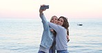 Two friends happily taking selfies with a cellphone at sunset during their holiday