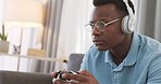 Video game, headphones and gamer man on sofa playing online, esports or virtual web competition. Game, young black man and modern gaming, wifi streaming twitch with controller and headset at home
