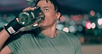 Black man, exercise and drinking water at night while tired against city background after training and boxing workout in city. Face of LA boxer with bottle to stay hydrated for fitness and kickboxing