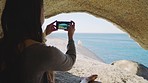 Beach, cave and woman with phone for picture, photography and memories of holiday, vacation and scenic view. Travel, smartphone and girl enjoying freedom, journey and adventure on rock by ocean 