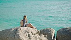 Woman, ocean and rock while on holiday and thinking about freedom, decision and travel with backpack and calm water outdoor in nature. Female tourist at Sydney beach on vacation for sea air and peace