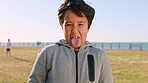 Cild, funny face and beach park with tongue out for disgust and gross facial expression in nature for fun, play and travel. Portrait of boy on vacation in Florida with comic emoji outdoor on grass