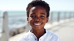 Black child, face and smile for happiness on a beach promenade while on summer travel vacation for fun, freedom and adventure outdoor. Portrait of boy kid from France showing teeth on holiday at sea