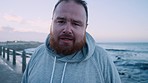 Face, front and active plus size man taking a workout break from running for weight loss. Cardio, break and portrait of a an overweight male athlete running by the ocean to lose weight 