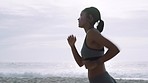 Woman, running and listening to music on beach sand in morning while outdoor for fitness, workout and cardio with strong mindset for speed and body goals. Athlete with earphones  for ocean air run