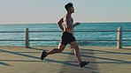 Running, beach fitness and man doing a sport, exercise and marathon training run at the sea. Workout, cardio and runner on a ocean sidewalk with speed and energy doing sports for health and wellness