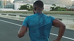 City, fitness or black man running on road in cardio training, workout or exercise to prepare for a fast sprinting race. Sprinter, back view or healthy athlete runner exercising with speed or focus