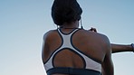 Fitness, exercise and back of black woman stretching and listening to music outdoor against blue sky for workout goals and cardio training. Female athlete outdoor for warm up to start running 