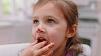 Girl eating with chocolate on happy face, messy hands and sitting in kitchen on weekend morning. Sweet treats, child with candy and fun dessert, chocolate bar or cookie with smile and mess in home.