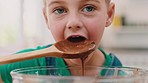 Chocolate, face and child eating dessert food from spoon to taste cake, muffin or sauce liquid in home kitchen while baking. Happy boy kid in UK house to lick cooking bowl while learning to bake