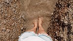 Top view, woman or feet by beach, ocean or sea in travel location, summer break or tropical holiday vacation. Tourist, legs or water washing pov on rocky sand in nature freedom, peace or zen wellness