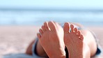 Feet, beach and summer with a woman lying on the sand by the sea or ocean while on holiday or vacation. Relax, legs crossed and foot sole with a female alone on the sunny coast during a getaway