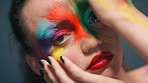 Woman, hands and face makeup in fine art, beauty or facial cosmetic paint against a studio background. Closeup portrait of beautiful female model with colorful skin art, vibrant paint or cosmetics