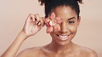 Face, flower and black woman with skincare, cosmetics and on brown studio background. African American female, girl or plant for natural beauty, organic treatment or soft skin for confidence or relax