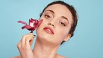 Skincare, orchid and beauty with woman on studio blue background for healthy skincare, wellness and luxury makeup in Colombia. Face, portrait and model with plant based flowers for natural treatment 