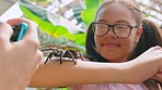Friend taking photo of tarantula spider on girl at zoo, park and excursion in nature for wildlife education, ecosystem and environment. Fearless youth with creepy insect on arm taking mobile picture