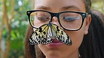 Child, butterfly park and smile on face outdoor in nature with glasses while on vacation for freedom, travel and peace while at a zoo. Portrait of teenager with animal on nose while happy and excited