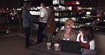Business people, talking and night on rooftop at office building in development, social or team building. Women, laptop or discussion on balcony with group, tablet or happy late in city of New York