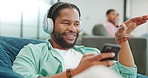 Headphones, phone and black man on a sofa in the living room dancing while listening to music. Relax, chill and African guy streaming radio, album or playlist while relaxing on a couch at his home.