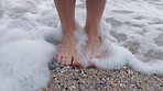 Beach, woman feet and standing in water for a tranquil and calm outdoor vacation break. Relaxation, paradise and barefoot while relaxing in ocean wave on summer holiday walk in sea sand.