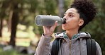 Hiking woman drinking water in nature, forest and mountain park for healthy lifestyle, wellness and outdoor adventure. Young black girl, water bottle and trekking, freedom and walk in morning woods