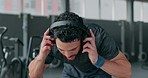 Rest, fitness and break by man at the gym after training cardio relax removing headphones or music. Sweat, fit and tired male athlete exercise as morning routine for health, wellness and motivation