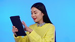 Asian woman, tablet and studio for communication, internet and social media on a blue background. Happy model person on mobile app for online chat, meme or laughing at funny post on website in studio