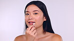 Face, lipstick makeup and beauty of Asian woman in studio isolated on a purple background. Skincare portrait, cosmetics kiss and happy female model laughing and apply product for beauty aesthetics.