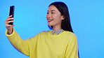 Asian woman, selfie and peace sign for social media profile picture on a blue background. Happy model person on mobile app for online chat, video call and blowing a kiss while flirting on smartphone