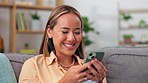 Asian woman, phone and smile relaxing on sofa for social media, chatting or texting in living room at home. Happy female smiling and typing on smartphone for chat, browsing or mobile app on the couch