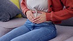 Stomach pain, cramps and woman hands in lounge with digestive and menstrual problem on a home couch. Constipation, tummy ache and abdomen health issue in a house on a sofa with bloating and ibs