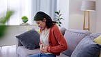 Pain, sick and woman feeling stomach for pregnancy, problem and insecurity. Sad, depression and Asian girl touching her belly for body dysmorphia, illness and pregnant abdomen on the lounge sofa