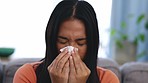 Sick, tissue and woman blowing her nose while sitting on a sofa in the living room of her home. Covid, illness and Asian female sneezing with flu, cold or allergies in the lounge of her modern house.