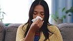 Illness, tissue and female blowing her nose while sitting on a sofa in the living room of her home. Covid, sick and Asian woman sneezing with flu, cold or allergies in the lounge of her modern house.