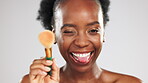 Face, makeup and funny with a black woman in studio on a gray background to apply blusher to her skin. Portrait, cosmetics and playful with an attractive young female laughing or winking for beauty