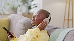 Black woman on couch, headphones and smartphone with connection, relax and streaming music in lounge. African American female, lady and cellphone with headset, listening to sounds and radio for songs