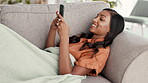 Woman, phone and chatting in relax on living room sofa for communication, texting or social media at home. Happy female lying on couch with smile typing on smartphone for networking, browsing or chat