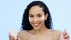 Face, cream and beauty of woman with cosmetics, smile and sunscreen on blue background. Facial skincare, lotion jar and portrait of happy model with product for shine, happiness and aesthetic makeup