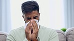 Tissue, sneeze and Indian man blowing nose on a home living room sofa feeling sick and tired. Allergy problem, virus and toilet paper of a person on a house lounge couch with sinus infection and flu