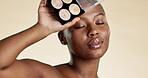 Black woman, face and makeup palette, beauty with eyeshadow or foundation and cosmetic product on studio background. Eyes closed, skin glow and mockup with cosmetics, powder and female model hand