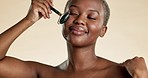 Beauty, black woman and face roller for cosmetics, wellness and treatment against a studio background. African American female, lady and rose quartz for glow, shine and smooth skin for confidence.