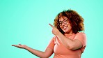 Face, pointing and black woman in studio with mockup space for promotion, advertising or announcement. Happy, smile and African female model showing mock up for product placement by blue background.