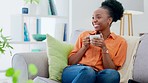 Coffee, happy and black woman relax on a sofa while laughing, watching and streaming in her home. Comic, entertainment and lady on a couch with tea, positive and chilling in a living room on day off