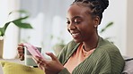 Coffee, phone and black woman relax on a sofa, happy and laughing at social media, text or meme in her home. Comic, online and girl with tea, smartphone or app, chatting or reading, post or meme 