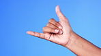 Hand, gesture and shaka with a person in studio on a blue background feeling carefree closeup. Emoji, sign and signal with an adult indoor to show a surfs up greeting on a pastel color wall